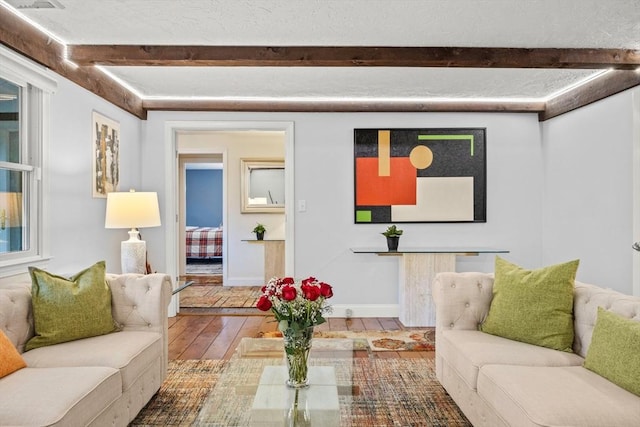 living area with a textured ceiling, hardwood / wood-style floors, beamed ceiling, and baseboards