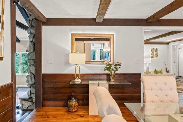 dining room with beam ceiling, wainscoting, wood walls, and wood finished floors