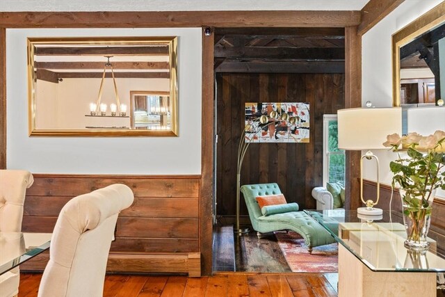 sitting room featuring wood-type flooring, a notable chandelier, wood walls, and beamed ceiling