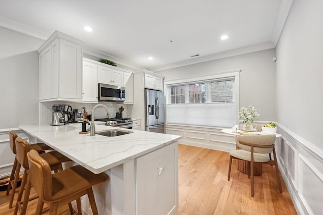 kitchen featuring sink, appliances with stainless steel finishes, white cabinets, a kitchen bar, and kitchen peninsula