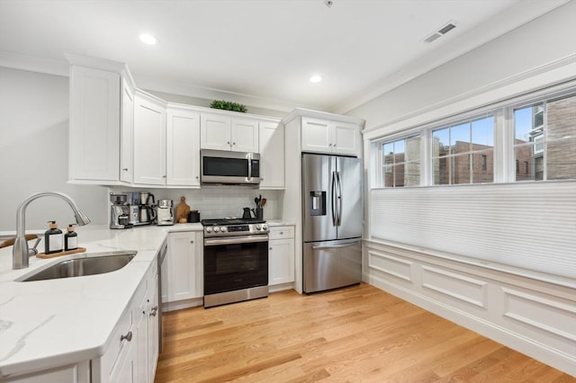 kitchen with stainless steel appliances, white cabinetry, sink, and light hardwood / wood-style floors