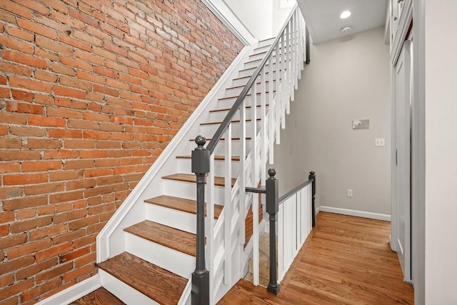 stairway featuring hardwood / wood-style flooring and brick wall