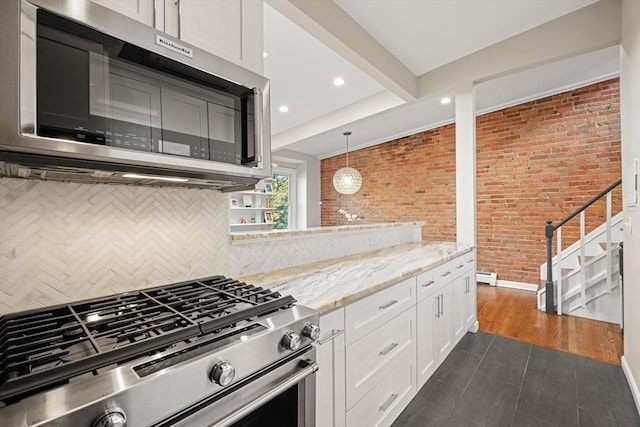 kitchen with brick wall, white cabinets, hanging light fixtures, stainless steel appliances, and light stone countertops