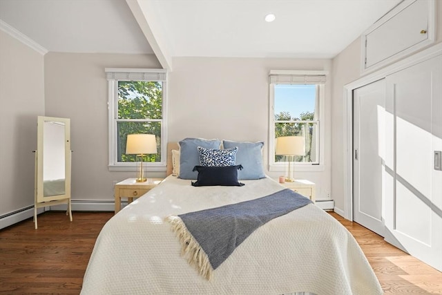 bedroom featuring multiple windows, a baseboard heating unit, and light wood-type flooring