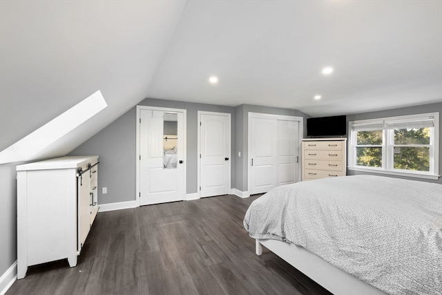 bedroom with multiple closets, dark hardwood / wood-style flooring, lofted ceiling with skylight, and a barn door