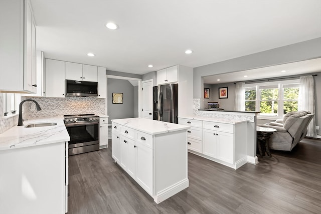 kitchen with a center island, stainless steel appliances, dark wood-type flooring, light stone counters, and white cabinets