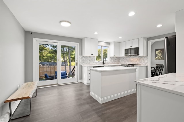 kitchen with tasteful backsplash, dark hardwood / wood-style flooring, light stone counters, a center island, and white cabinets