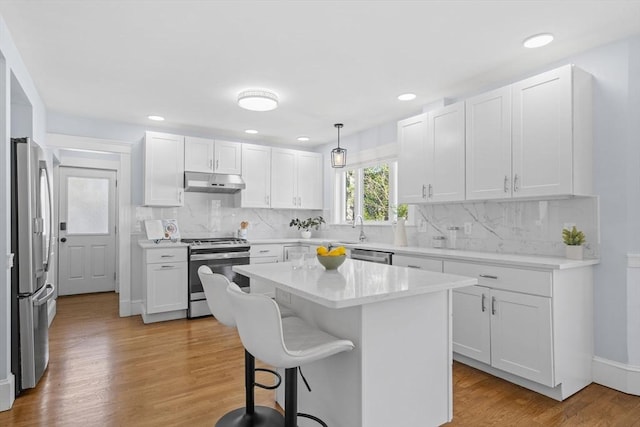 kitchen with a breakfast bar, light countertops, white cabinetry, under cabinet range hood, and appliances with stainless steel finishes