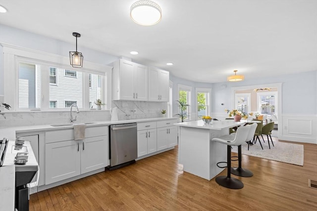 kitchen with a breakfast bar area, wood finished floors, dishwasher, a sink, and white cabinetry