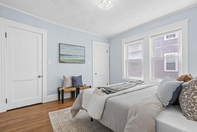 bedroom featuring baseboards, ornamental molding, wood finished floors, and an inviting chandelier