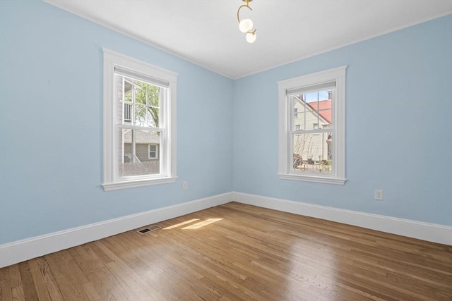 spare room with baseboards, visible vents, and wood finished floors