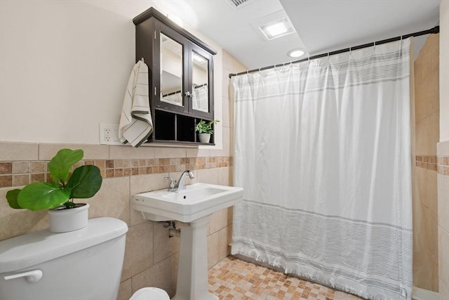 bathroom with toilet, a shower with curtain, tile walls, and visible vents