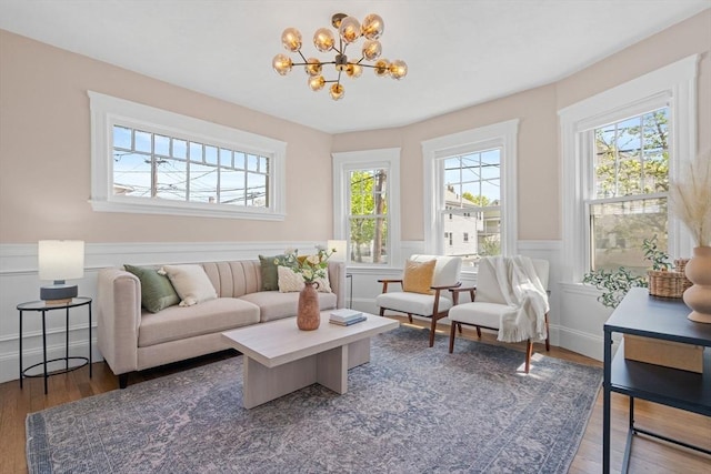 living room with a decorative wall, wainscoting, wood finished floors, and a chandelier