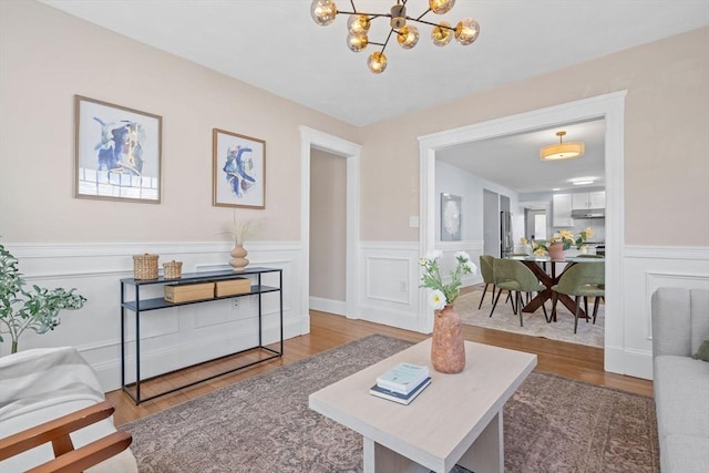 living area featuring a decorative wall, a chandelier, wood finished floors, and a wainscoted wall