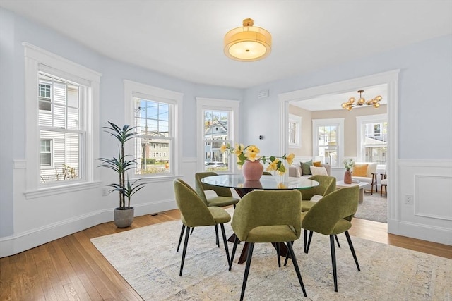 dining room with an inviting chandelier, a wealth of natural light, hardwood / wood-style flooring, and a wainscoted wall