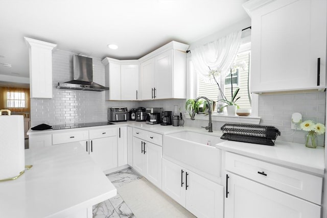 kitchen featuring marble finish floor, black electric stovetop, light countertops, a sink, and wall chimney range hood