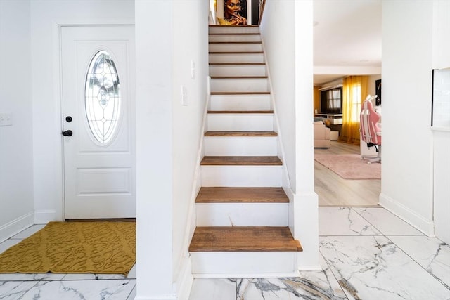 entryway featuring marble finish floor, baseboards, and stairs