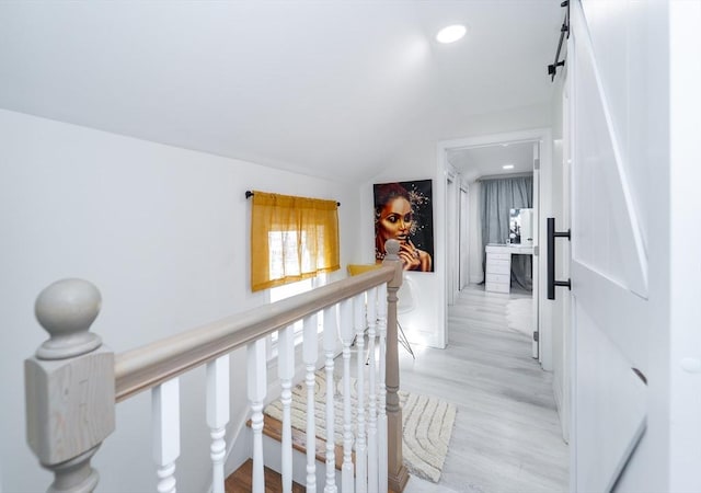 corridor with light wood finished floors, a barn door, lofted ceiling, an upstairs landing, and recessed lighting