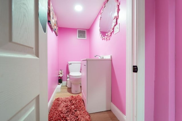 half bathroom with baseboards, vanity, toilet, and wood finished floors