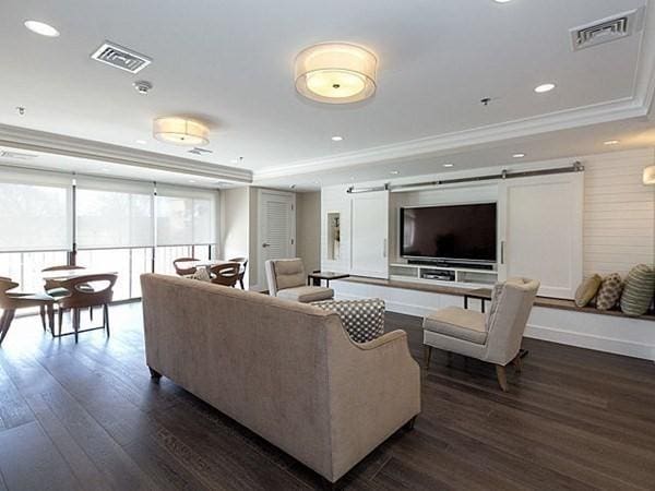 living room with ornamental molding, a barn door, dark wood-type flooring, and a tray ceiling