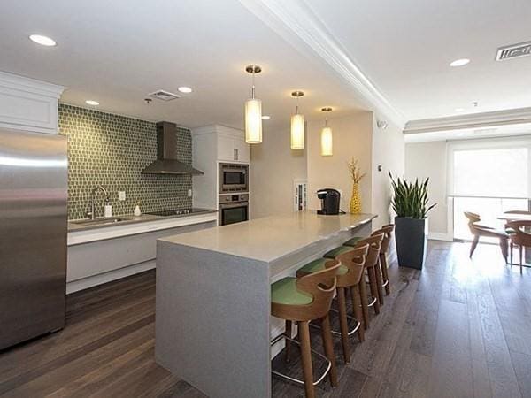 kitchen featuring pendant lighting, wall chimney range hood, sink, appliances with stainless steel finishes, and white cabinets