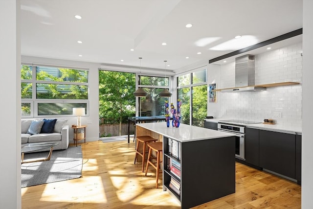 137 Walden St Unit 137, Cambridge, MA 02140 - kitchen featuring dark cabinetry, wall chimney exhaust hood, a center island, oven, and light countertops