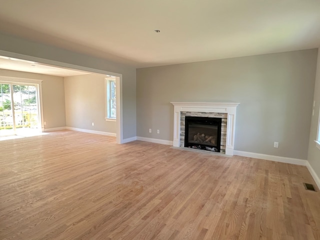 unfurnished living room featuring light hardwood / wood-style flooring and a stone fireplace