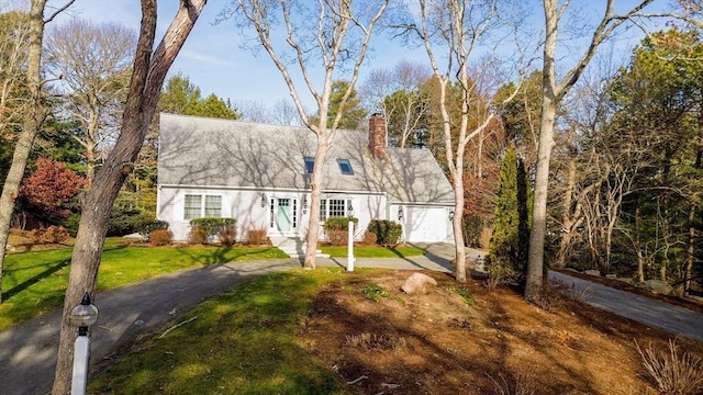 new england style home with aphalt driveway, a garage, a chimney, and a front yard