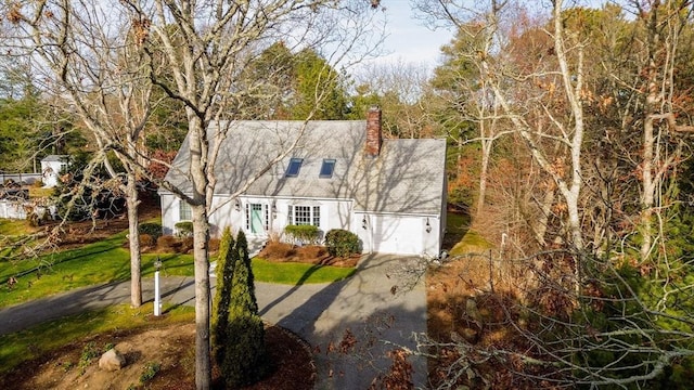 cape cod-style house featuring a garage, a chimney, and driveway