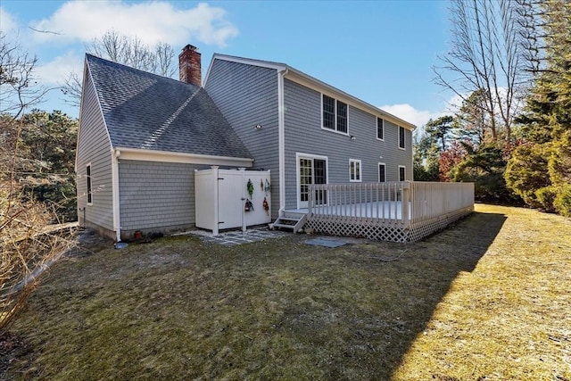 back of house with a yard, roof with shingles, a deck, and a chimney