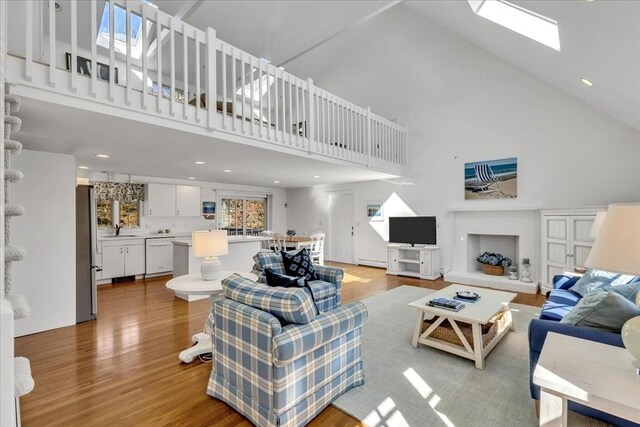 living room featuring baseboard heating, a skylight, light wood-type flooring, and a high ceiling