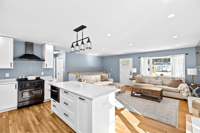 kitchen with light wood-type flooring, black gas stove, light countertops, wall chimney range hood, and open floor plan