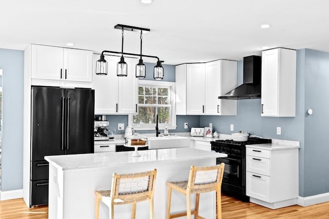 kitchen featuring black appliances, a sink, a breakfast bar area, wall chimney exhaust hood, and white cabinets