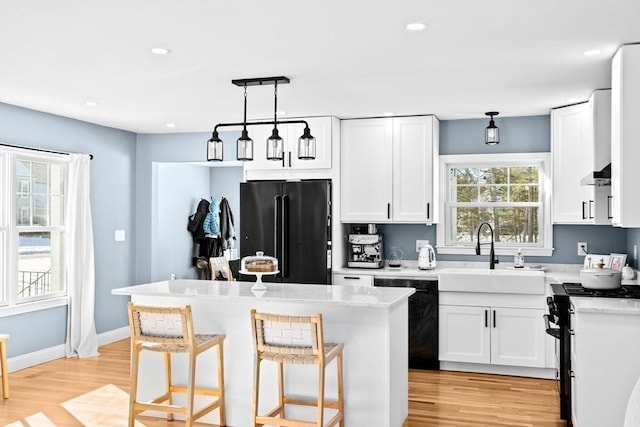 kitchen featuring light wood-type flooring, black appliances, a sink, white cabinets, and hanging light fixtures