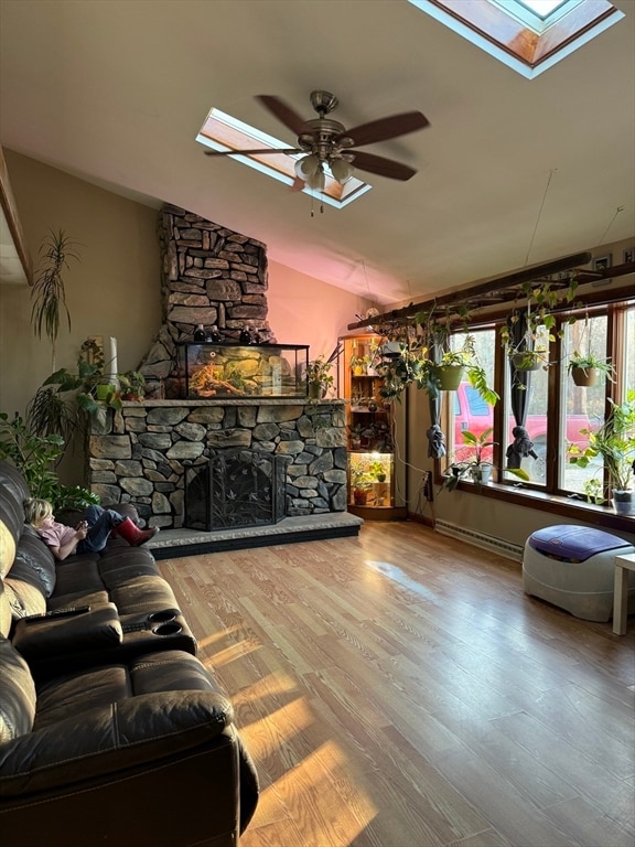 living room featuring wood-type flooring, a stone fireplace, ceiling fan, and vaulted ceiling with skylight