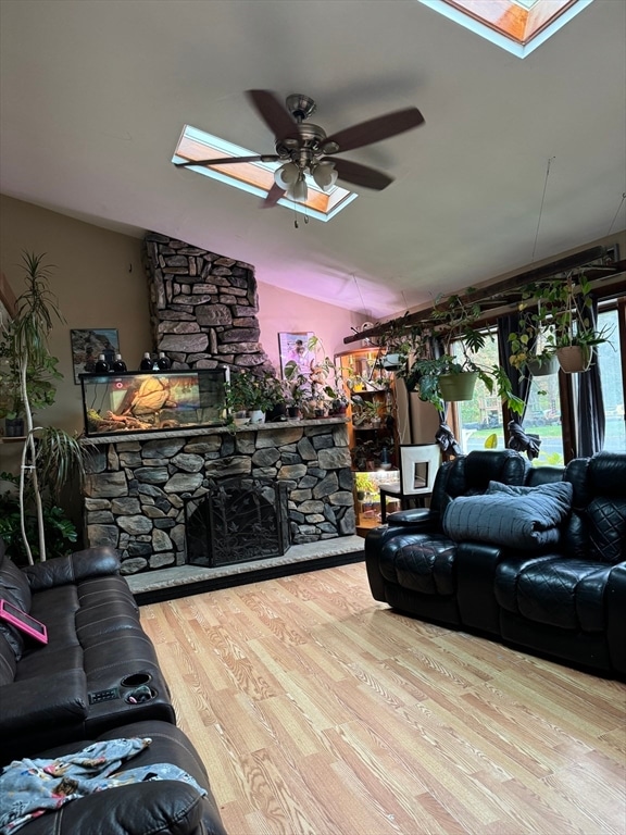 living room featuring light hardwood / wood-style flooring, lofted ceiling with skylight, ceiling fan, and a stone fireplace