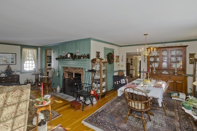 dining room with hardwood / wood-style floors, ornamental molding, a chandelier, and a brick fireplace