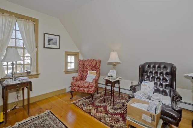 living area featuring hardwood / wood-style flooring, a baseboard radiator, a healthy amount of sunlight, and vaulted ceiling