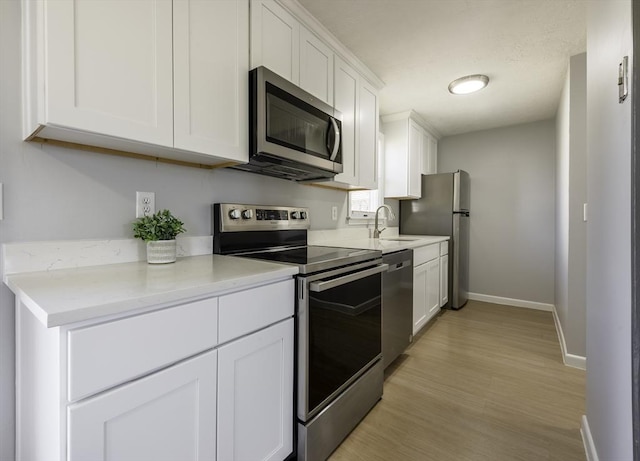 kitchen featuring white cabinets, appliances with stainless steel finishes, a sink, baseboards, and light wood-type flooring