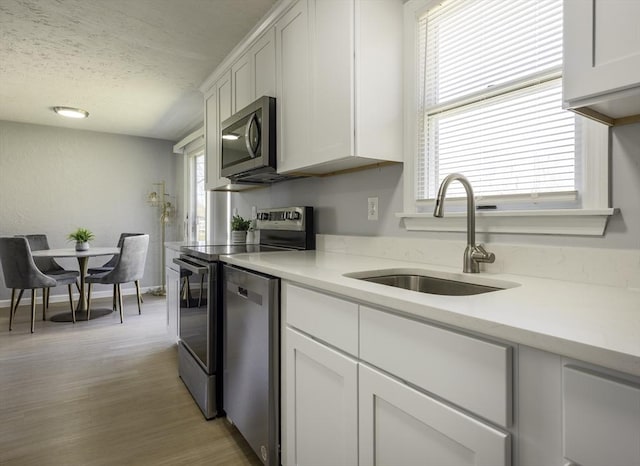 kitchen featuring a sink, a textured ceiling, appliances with stainless steel finishes, and white cabinets
