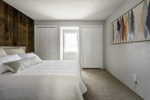 carpeted bedroom with a textured ceiling, multiple closets, a textured wall, and wood walls