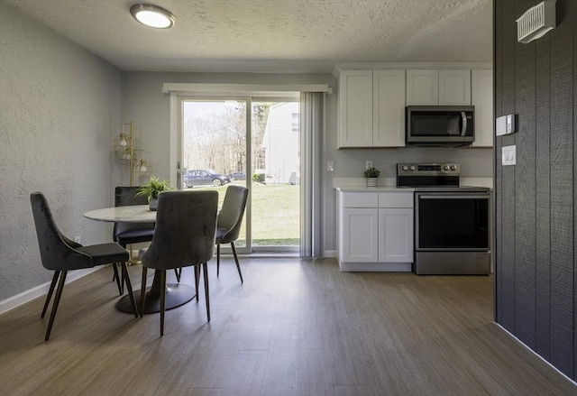 dining room featuring a textured ceiling, visible vents, wood finished floors, baseboards, and a textured wall