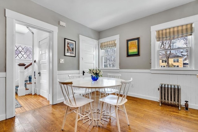 dining area with light wood finished floors, radiator, a wealth of natural light, and wainscoting