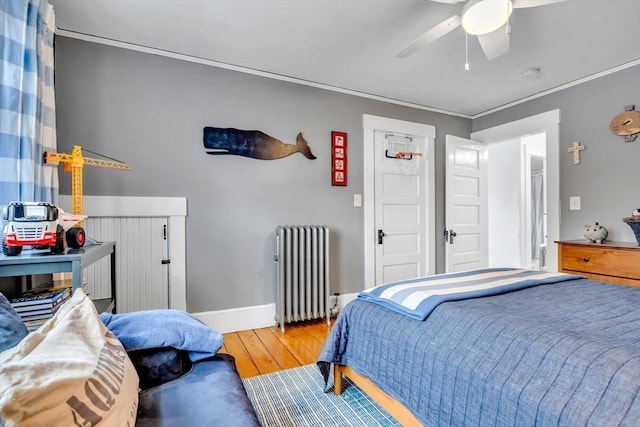 bedroom featuring a ceiling fan, baseboards, radiator heating unit, wood-type flooring, and crown molding