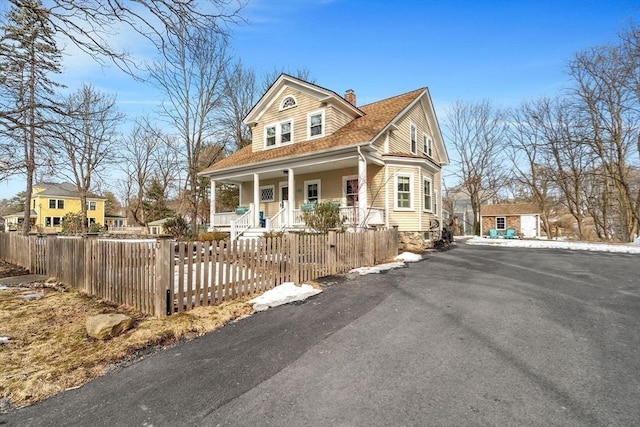 view of front of home with a shingled roof, covered porch, a fenced front yard, and a chimney