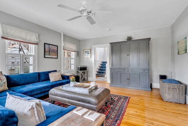 living area featuring plenty of natural light, ceiling fan, stairs, and light wood-style floors