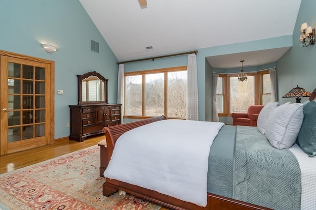 bedroom featuring high vaulted ceiling, a chandelier, hardwood / wood-style flooring, and multiple windows