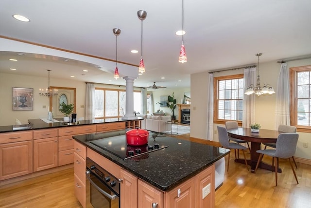 kitchen with black electric cooktop, dark stone countertops, hanging light fixtures, oven, and light hardwood / wood-style flooring