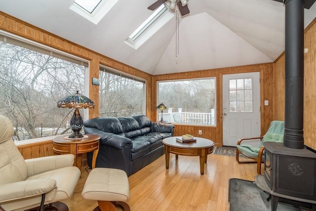 sunroom with ceiling fan, plenty of natural light, a wood stove, and lofted ceiling with skylight