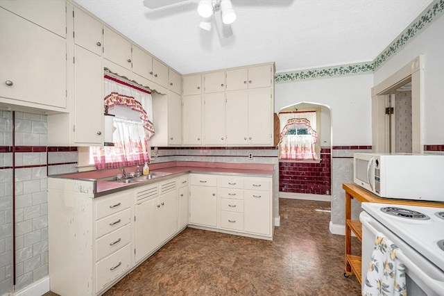 kitchen with ceiling fan, wainscoting, a sink, white appliances, and tile walls